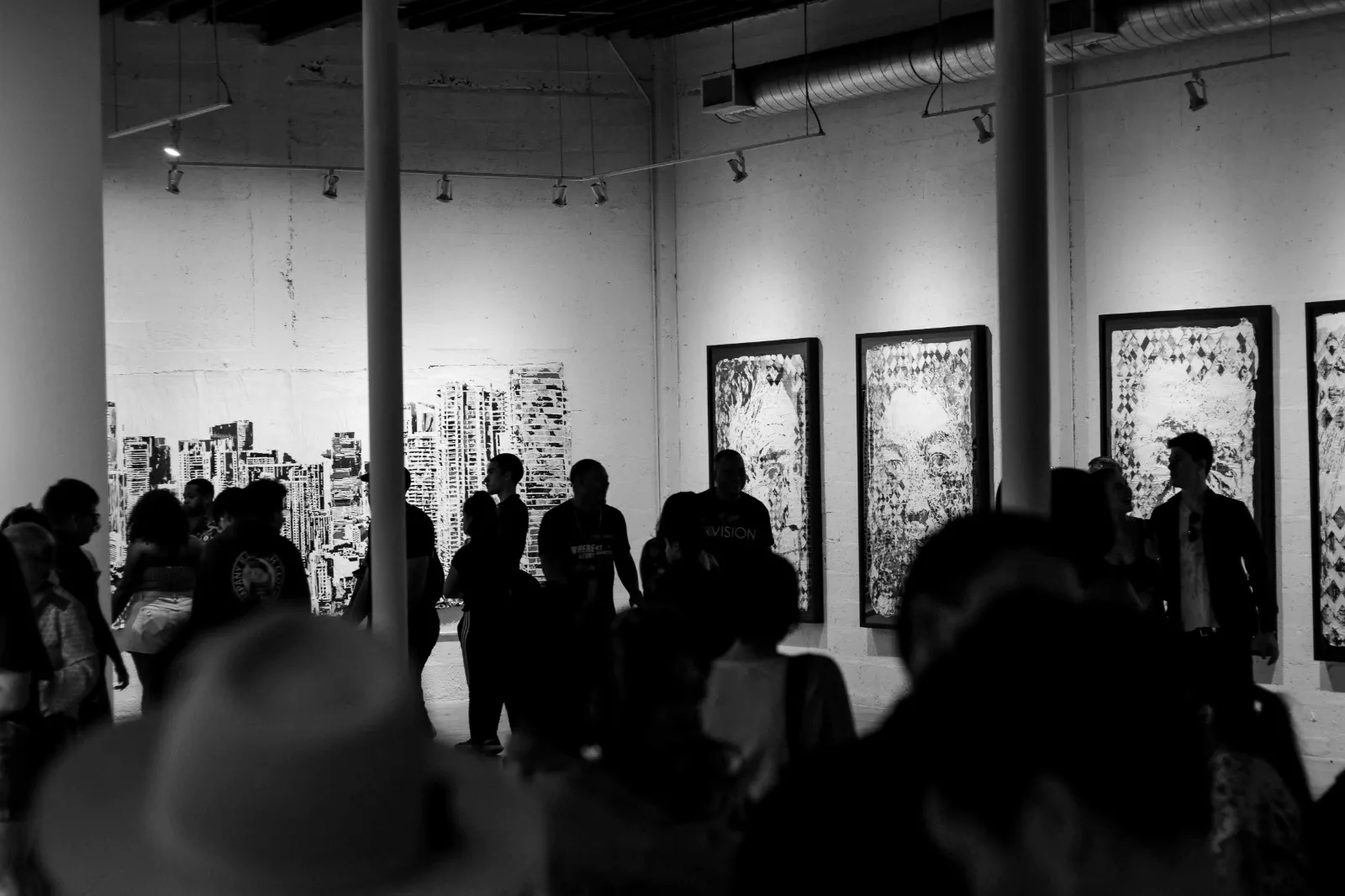 Visitors at an art exhibition viewing framed works and a painted cityscape